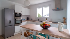 A modern kitchen with white cabinets, a stainless steel refrigerator, an oven, a microwave, a sink, and a window providing natural light. - Villa Ti Vakansou - Avec piscine privée (Clohars-Carnoët)