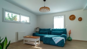 A modern living room with a teal sofa, a wooden coffee table, and a hanging wicker light fixture. - Villa Ti Vakansou - Avec piscine privée (Clohars-Carnoët)