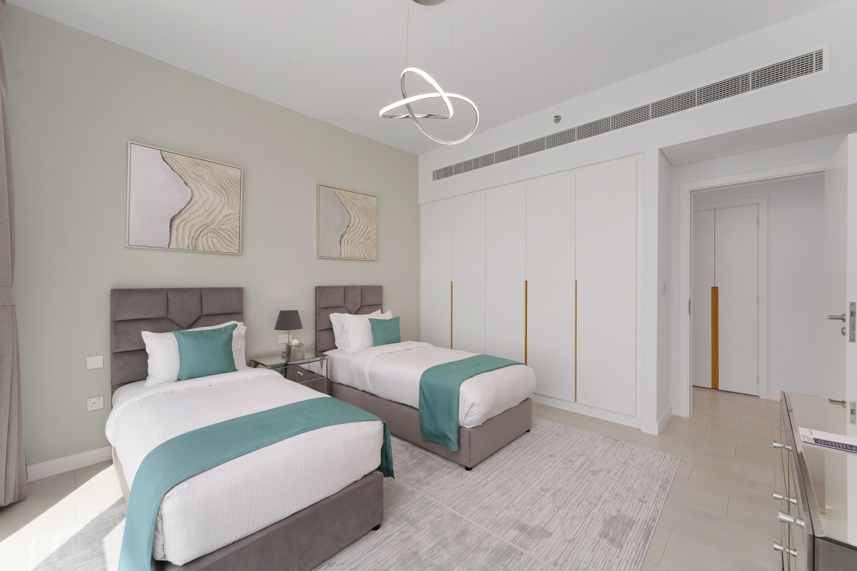 A modern bedroom with two beds, a large wardrobe, and a desk.