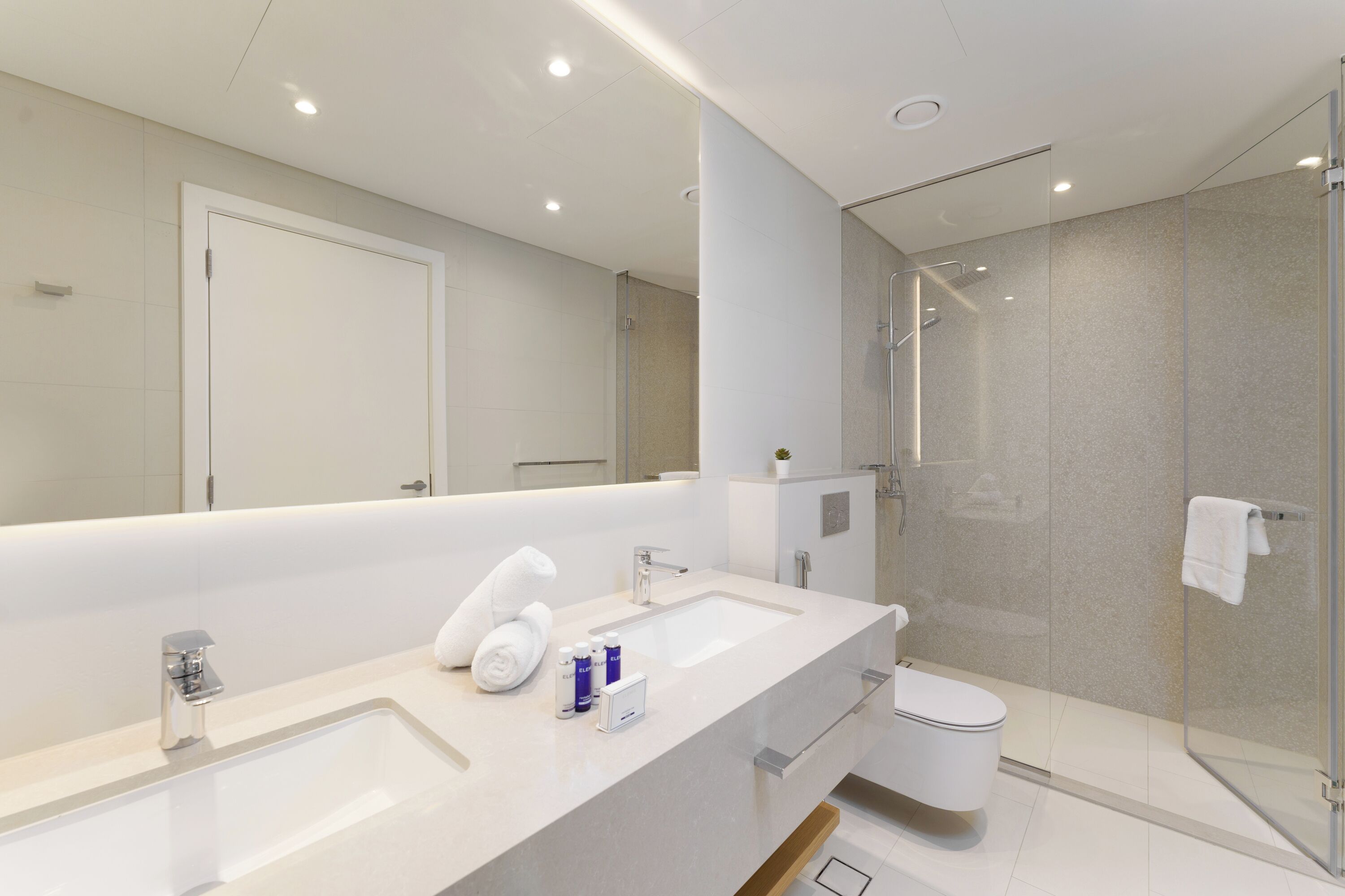 Une salle de bain moderne avec un grand miroir, un lavabo, des toilettes et une douche à parois de verre.