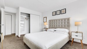 Un dormitorio ordenado con una cama grande, mesitas de noche, un armario y un espejo.