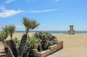 A beach with a lifeguard tower, palm trees, and a clear sky.