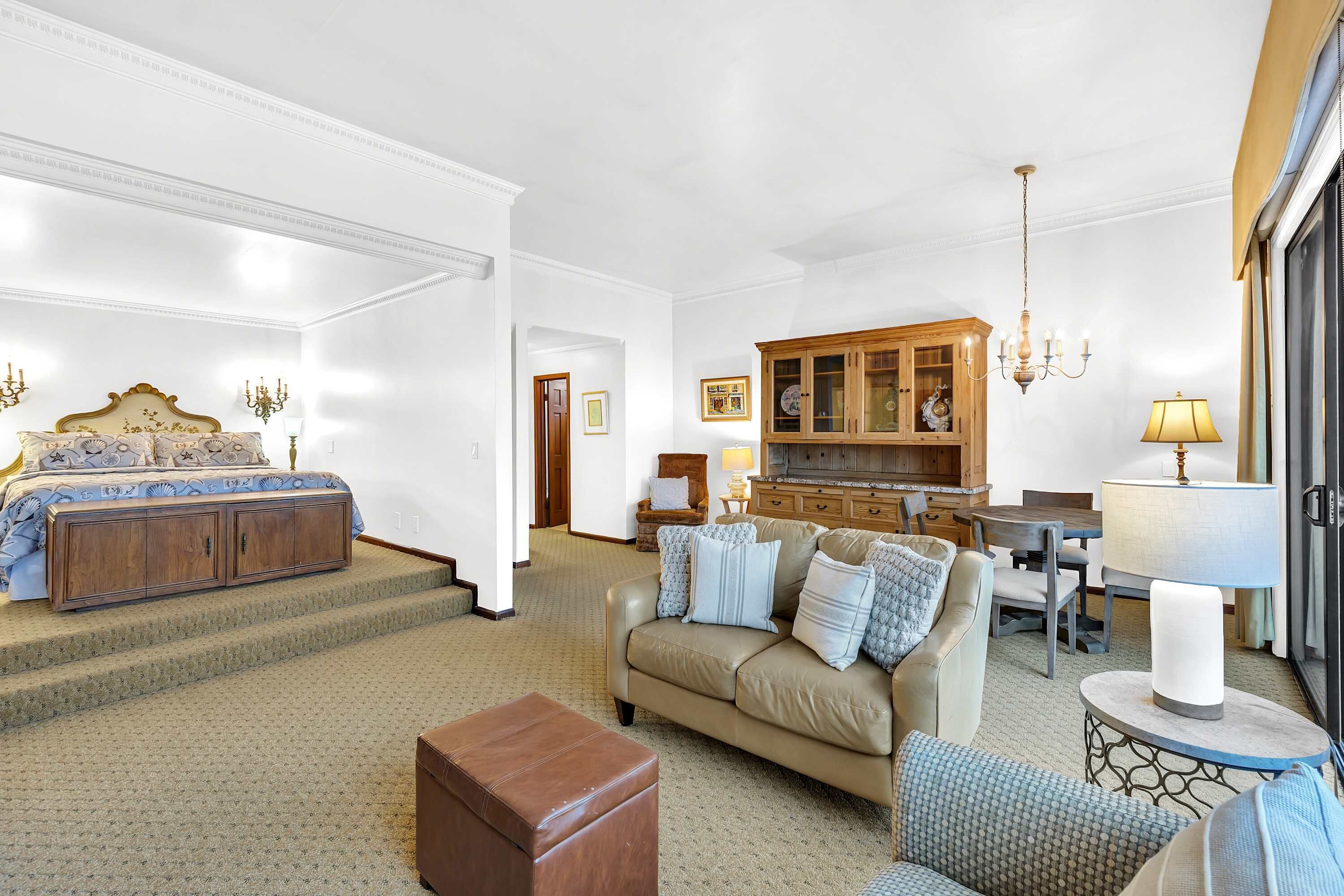 A hotel room with a bed, a sofa, a dining area, and a kitchen.