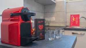 A red Nespresso coffee machine, a box of Nespresso Mediterranea capsules, and three clear glasses on a kitchen counter. - Casa Delia by Wonderful Italy (Turin)