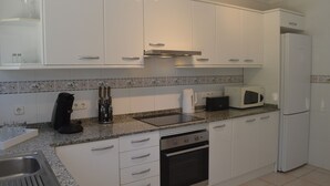 Una cocina moderna con armarios blancos, encimera de granito, horno empotrado, microondas y cafetera.