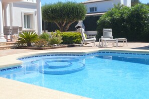 A swimming pool with a circular design, surrounded by white lounge chairs and a well-maintained garden.