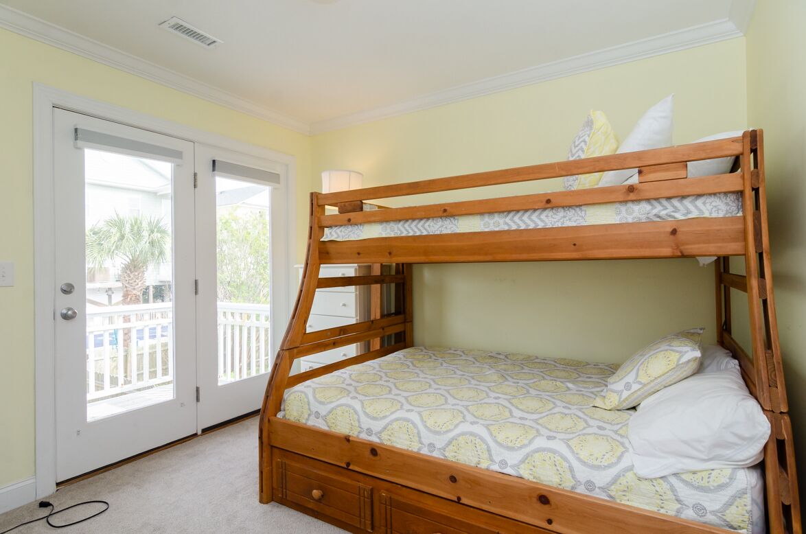 A bunk bed with a patterned bedspread, a wooden headboard, and a white door with a view of a balcony.
