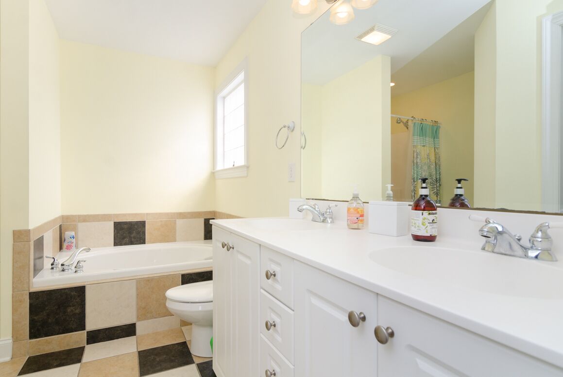 A bathroom with a white bathtub, a toilet, and a sink with a large mirror.