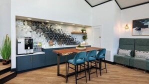 A modern kitchen with a hexagonal tile backsplash, a wooden dining table with four chairs, and a green sofa in the adjacent living area.