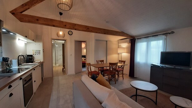 A modern kitchen with a dining area, a sofa, and a TV.