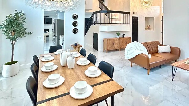 Una sala de estar moderna con comedor, que presenta una mesa de madera dispuesta con platos blancos y una araña.