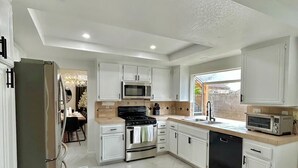 Una cocina moderna con armarios blancos, un refrigerador de acero inoxidable, un microondas, un horno y un lavavajillas.