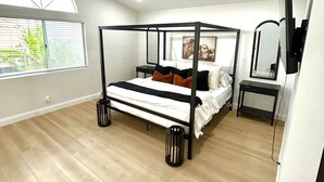 Un dormitorio con cama con dosel, ventilador de techo, ventana grande con persianas y televisor sobre un soporte.