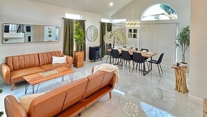 Amplia sala de estar con un sofá grande, una mesa de comedor con sillas y una araña.