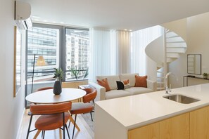 Un apartamento moderno con cocina, comedor y sala de estar. Cuenta con una escalera en espiral, ventanas amplias y vistas a la ciudad.
