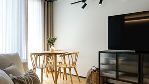 Un soggiorno moderno con un divano, un tavolo da pranzo con sedie, una TV su un mobile basso e un'ampia finestra con tende.
