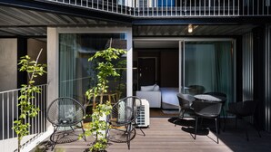 Patio esterno moderno con pavimento in legno, due sedie nere in rete metallica, un tavolino e un divano bianco.