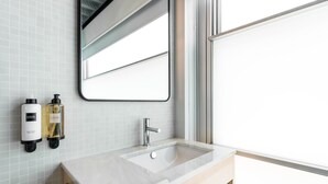 Un baño moderno con un espejo grande, un lavamanos rectangular y dos botellas de loción en la pared.