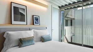 Une chambre d’hôtel moderne avec un grand lit, une tête de lit et une vue sur un balcon en verre.