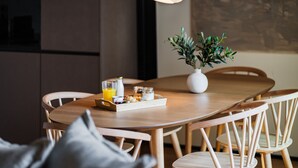 Une table de salle à manger en bois, sur laquelle se trouve un plateau contenant divers éléments pour le petit-déjeuner, notamment un verre de jus d’orange, une bouteille et une petite plante.