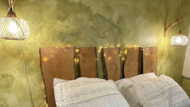 A bed with patterned bedding, a wooden headboard with string lights, and a textured green wall.