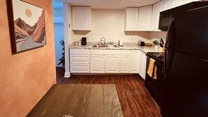 A compact kitchen with white cabinets, a black refrigerator, and a painting on the wall.