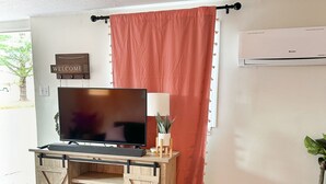 A living room with a wooden entertainment unit, a flat-screen TV, a red curtain, and a potted plant.