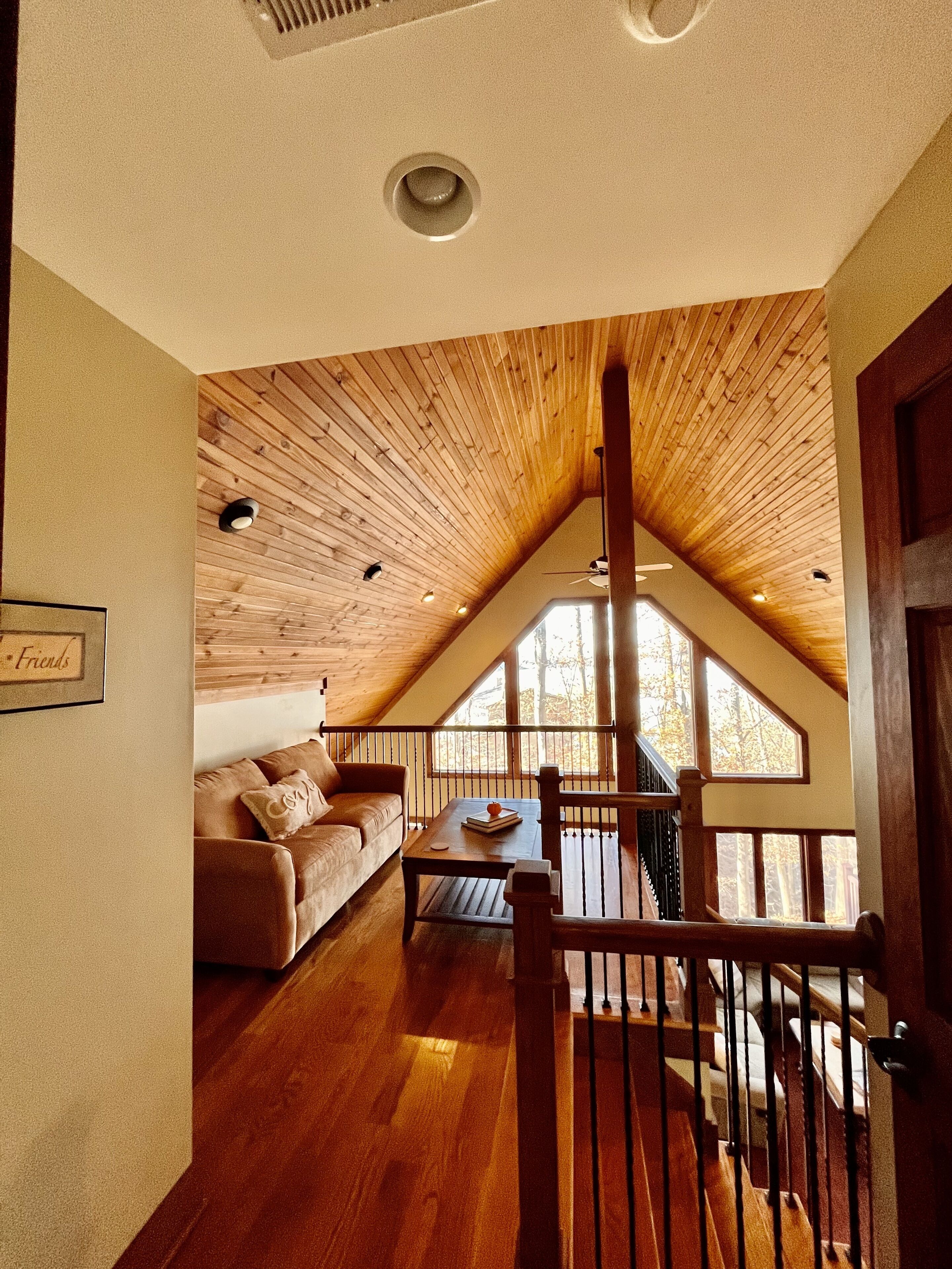Une pièce chaleureuse de style loft, avec un plafond en pente, un plancher en bois, un canapé, une table basse et un escalier menant à un niveau supérieur.