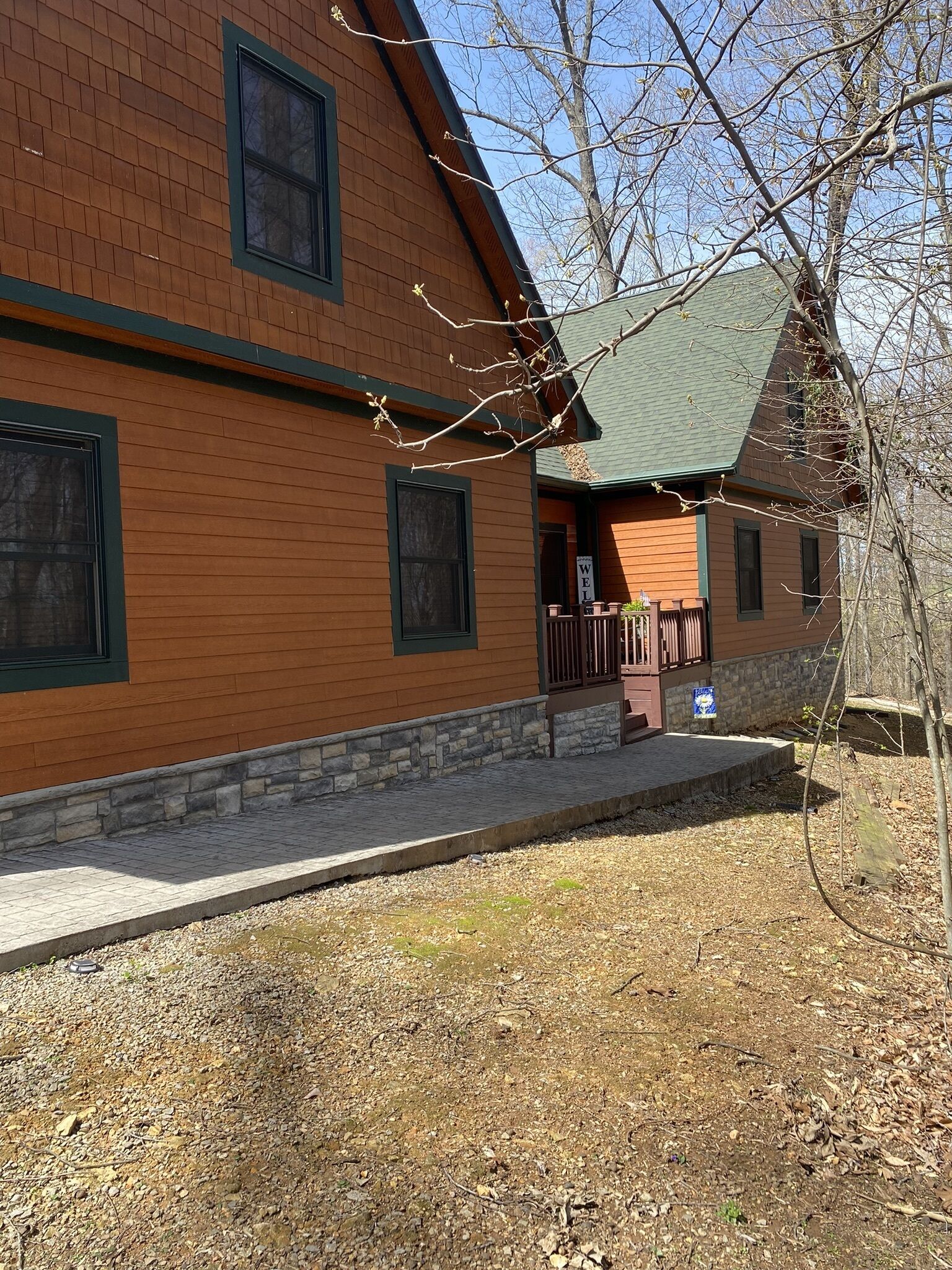 A two-story wooden house with a stone foundation, a porch with wooden railings, and a 'WELCOME' sign.