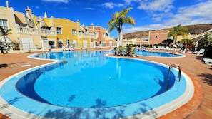A large outdoor swimming pool with multiple lanes, surrounded by palm trees and lounge chairs. - Superbe Duplex Avec vue mer - Jacuzzi, Jardin & Terrasse Privés (Palm-Mar)
