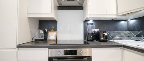 A modern kitchen with white cabinets, a built-in oven, a coffee maker, and a blender on the countertop.