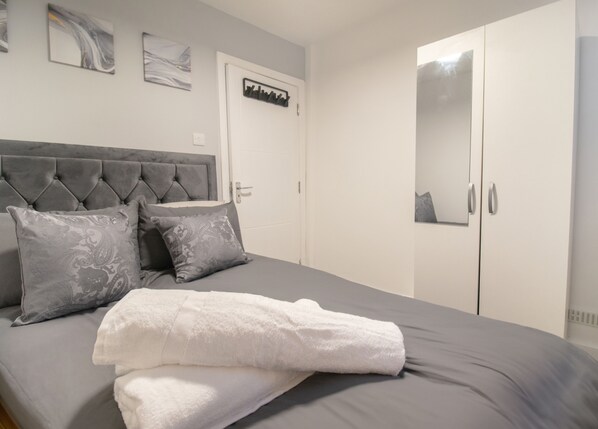 Ein Schlafzimmer mit einem grauen Bett, weißen Vorhängen und einem Kleiderschrank.