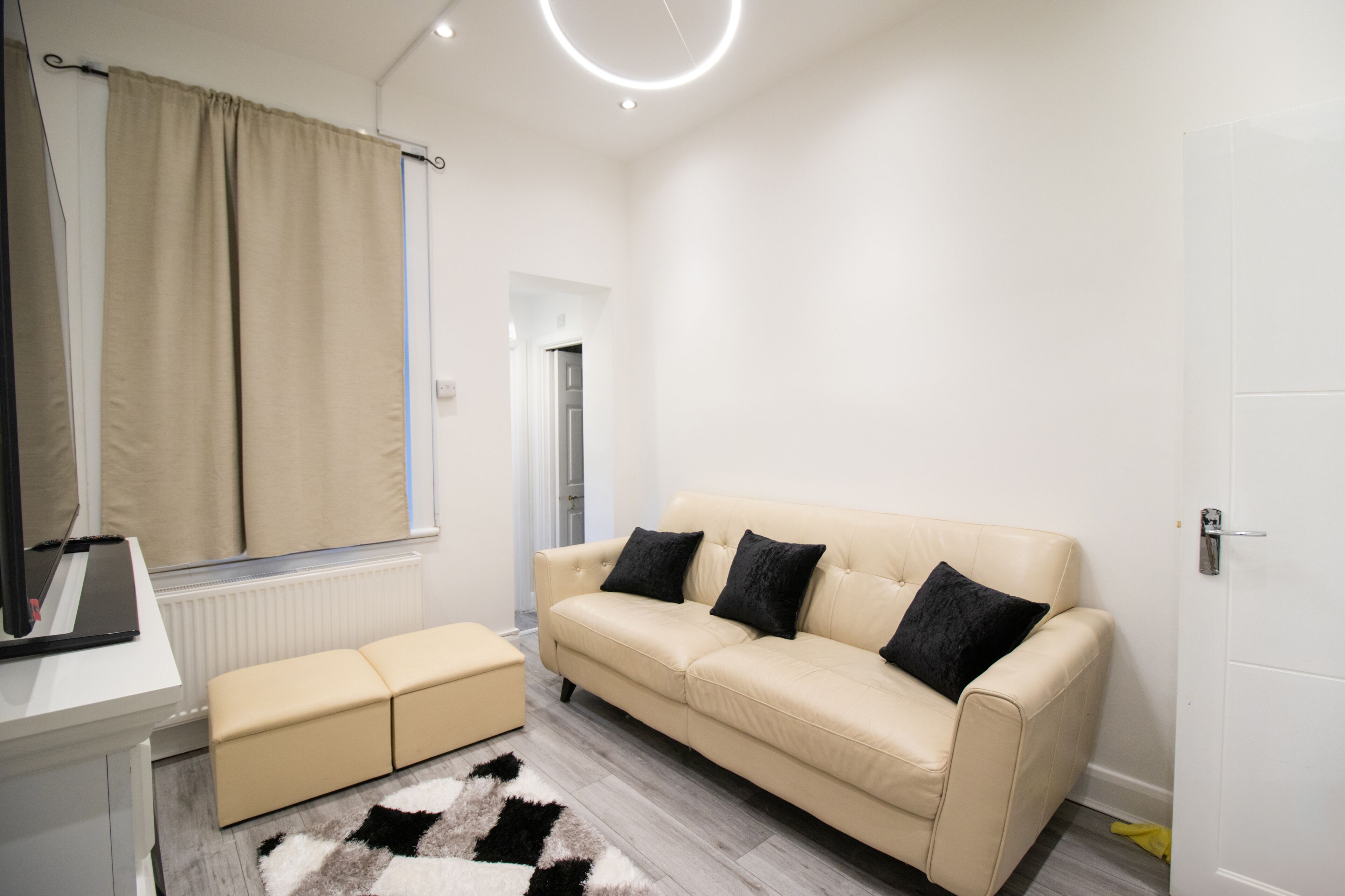 A modern living room with a beige sofa, a small ottoman, a round mirror, and a fluffy rug.
