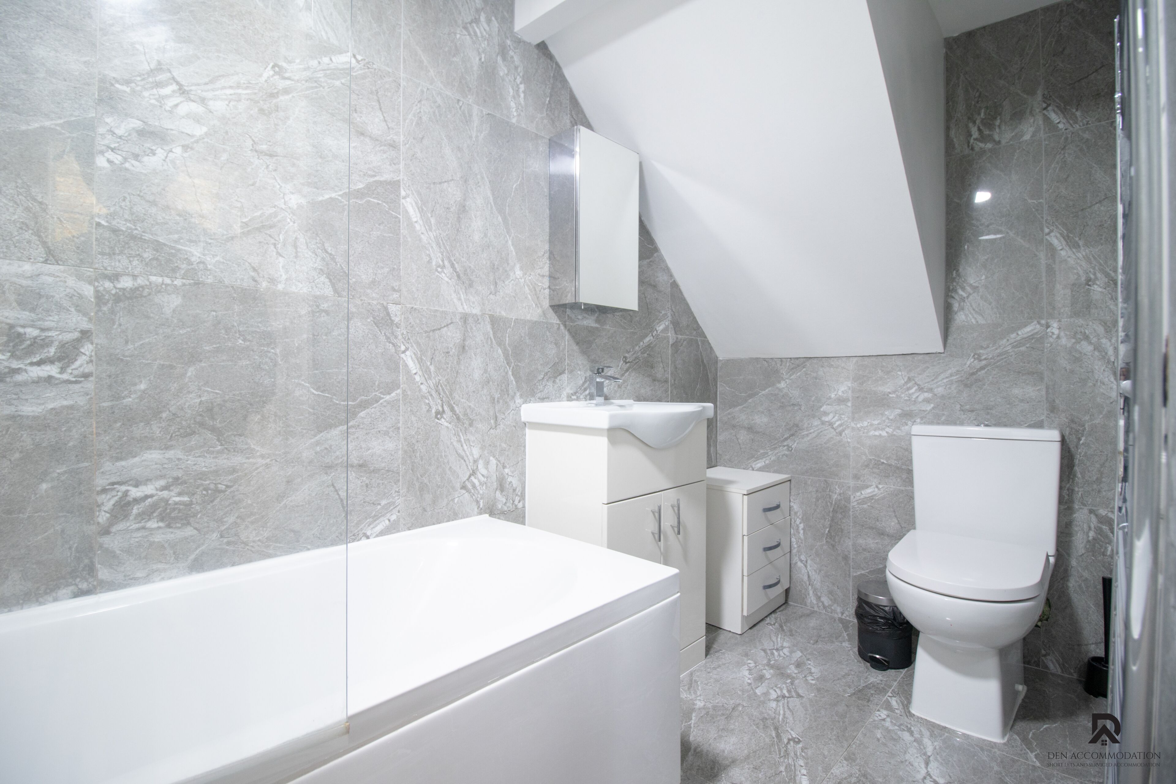 A modern bathroom with a marble floor, a white bathtub, a sink, a toilet, and a mirror.