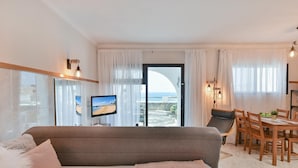 A modern hotel room with a large bed, a dining area, and a view of the sea.