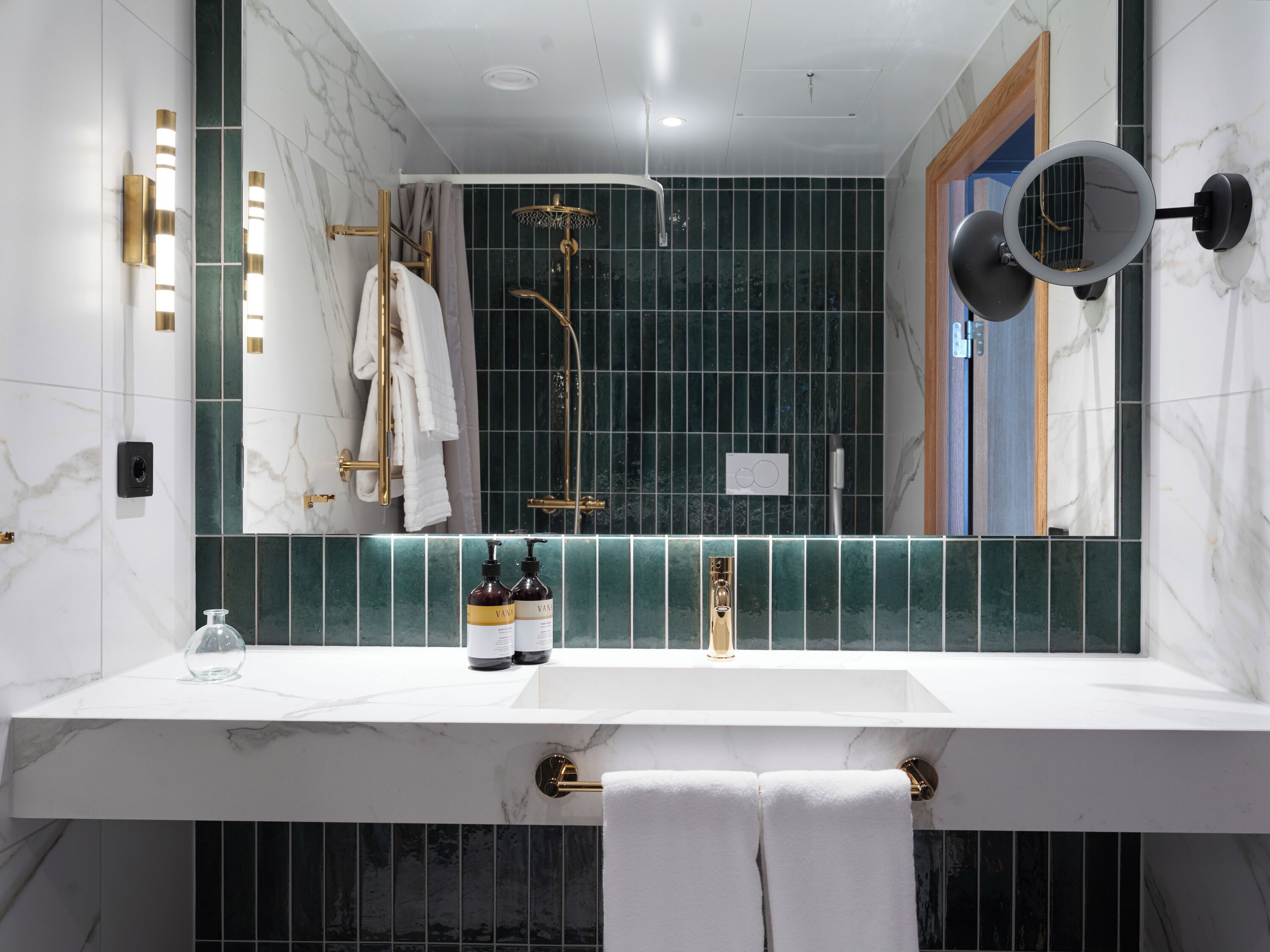 A modern bathroom with a white sink, gold fixtures, and green tiles.