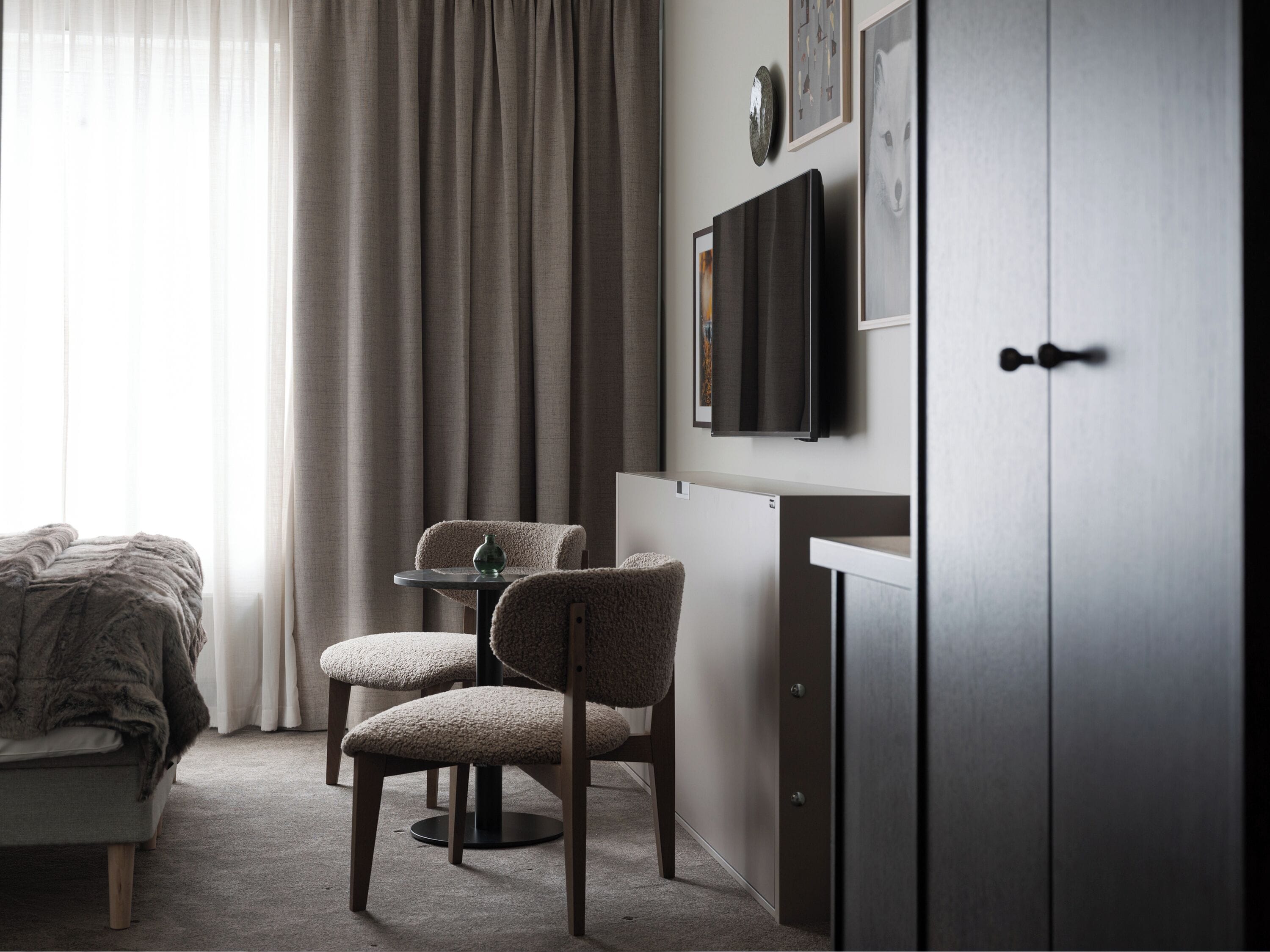 A modern bedroom with a bed, two chairs, a small table, a TV, and a wardrobe.