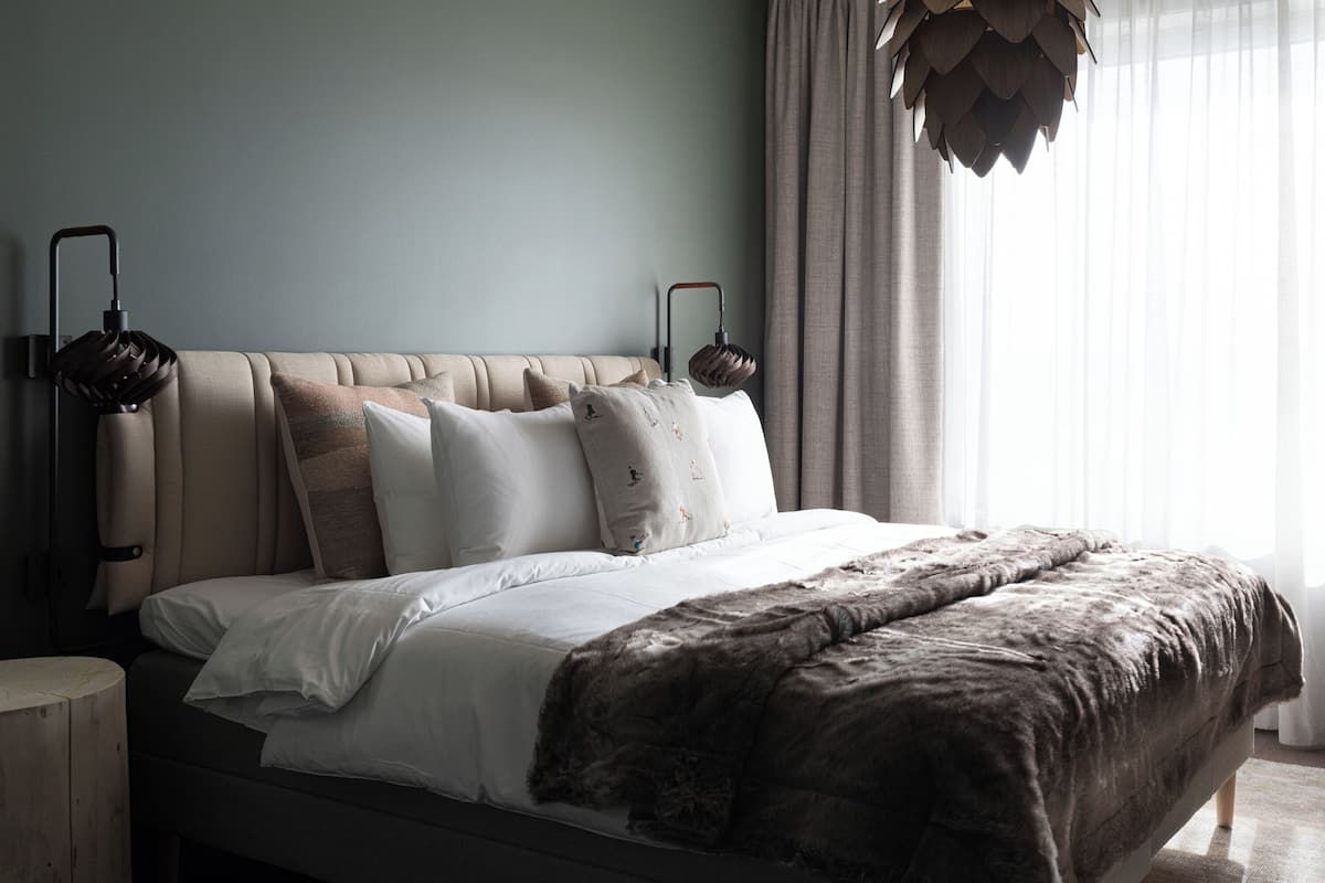 A bedroom with a large bed, a wooden nightstand, and a hanging light fixture.
