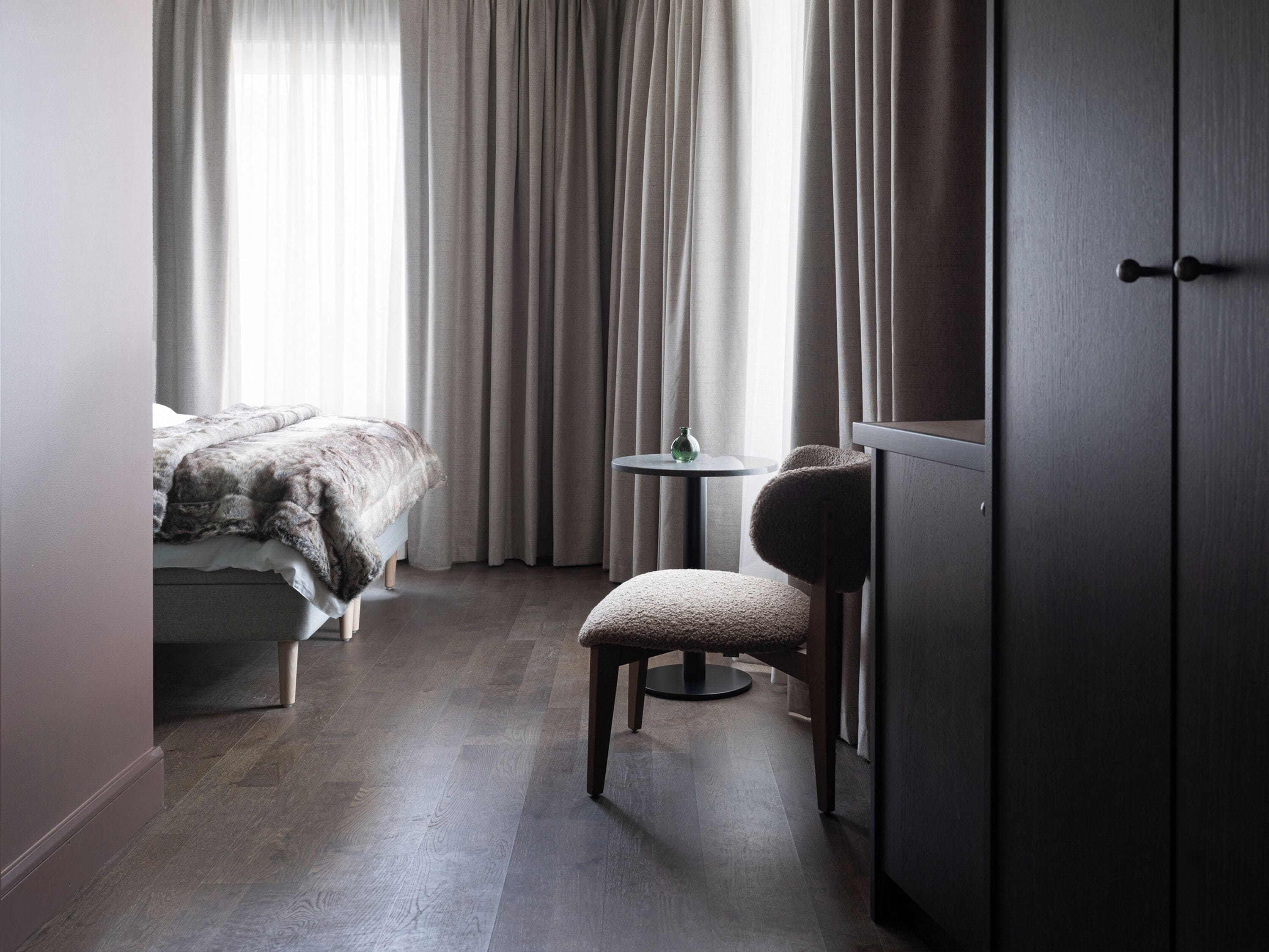 A bedroom with a bed, a chair, a small table, and a wardrobe.