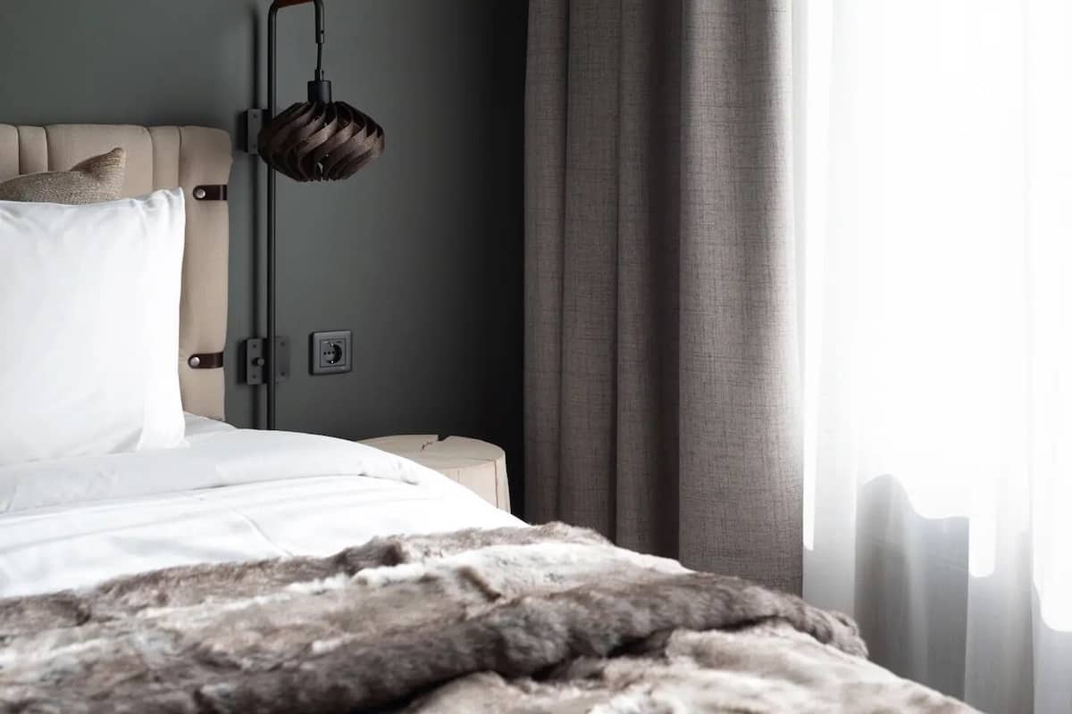 A bedroom with a bed, a bedside table, a lamp, and a window with curtains.
