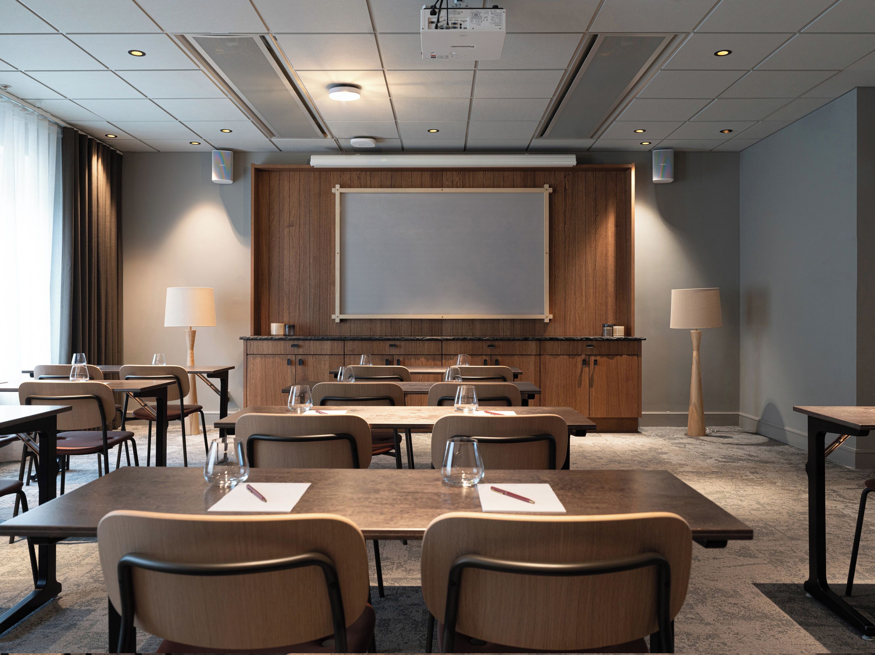 A conference room with a large projection screen, wooden cabinets, and multiple tables and chairs.