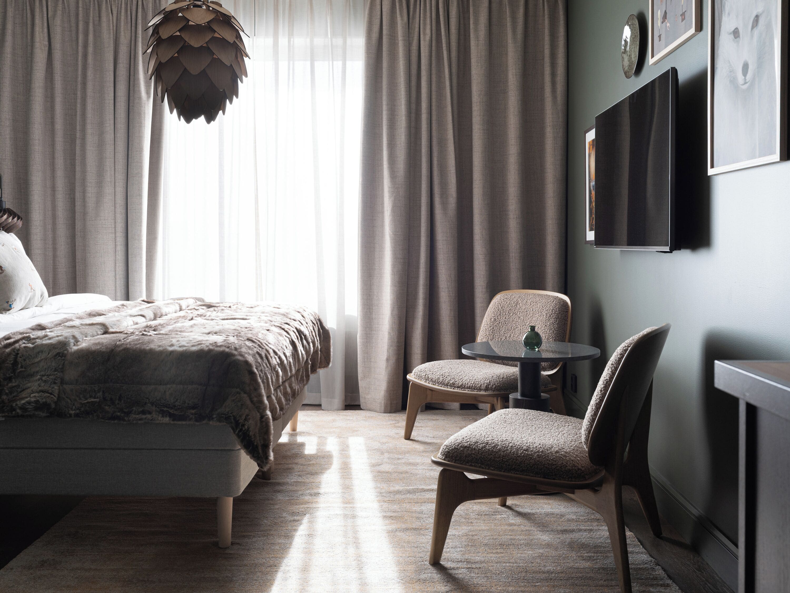 A modern bedroom with a large bed, a chair, a small table, and a TV mounted on the wall.