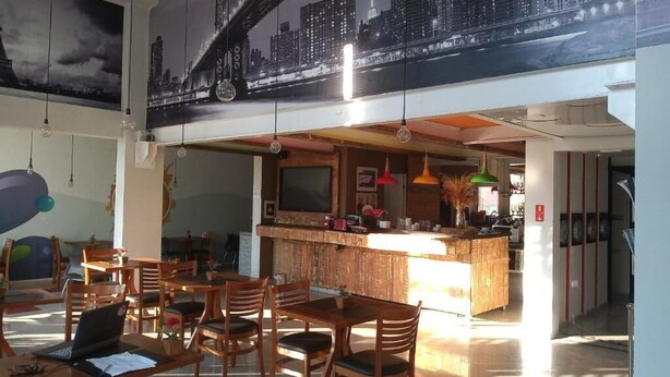 Un restaurante con mesas y sillas de madera, una zona de bar y un mural con un paisaje urbano en la pared.