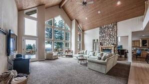 Amplia sala de estar con techos altos, ventanas grandes, chimenea de piedra y un rincón de asientos acogedor.