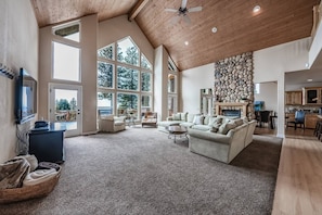A spacious living room with a high ceiling, large windows, a stone fireplace, and a cozy seating area.