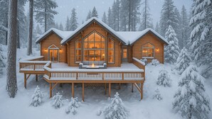 Una cabaña de troncos con terraza y ventanas amplias, rodeada de árboles cubiertos de nieve.