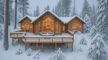 Une cabane en rondins dotée d’une terrasse et de grandes fenêtres, entourée d’arbres couverts de neige.