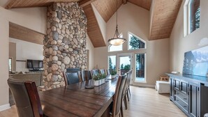 Un comedor amplio con pared de piedra, techo de madera y ventanas grandes.