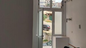 A narrow hallway with a glass door leading to a balcony. A small table with a broom and a bag is visible on the balcony. - Casa Mia Hostel SR (Sarandë)