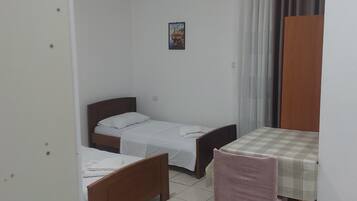 A small, clean room with two single beds, a wooden table with a checkered tablecloth, a chair, and a picture on the wall.